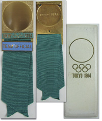 Offizielles Teilnehmerabzeichen Tokyo 1964 Team Official. Bronze, vergoldet. Schriftleiste hellblau emailliert mit grnem Seidenband, 14x3,8 cm. In original Prsentationsbox.<br>-- Schtzpreis: 240,00  --